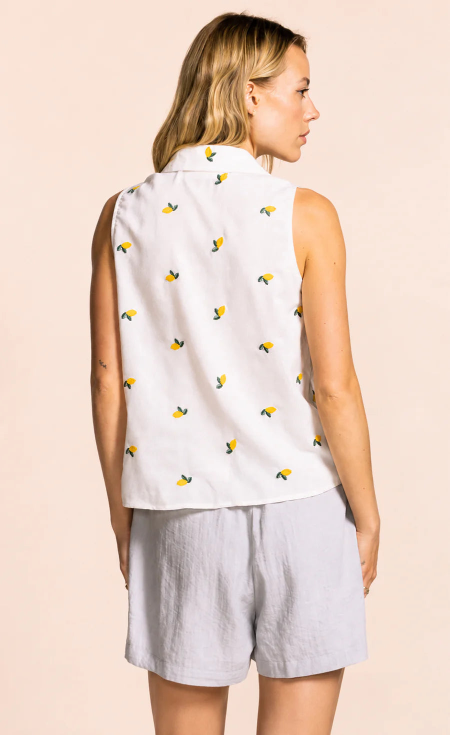 Woman wearing a sleeveless top with bee pattern and light shorts on a beige background