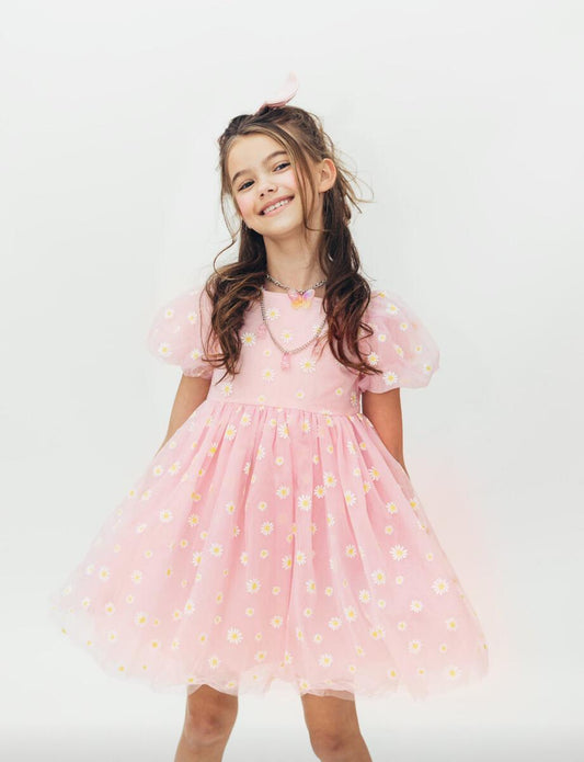 A young girl wearing a short-sleeved pink tulle dress with a daisy puff  design by Lola and the Boys.