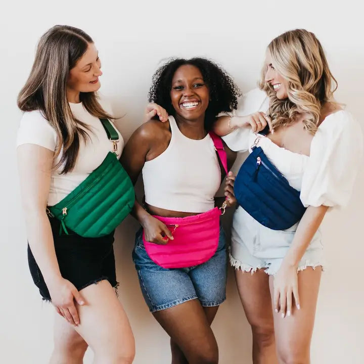 Three models wearing colorful cross body bags. Each bag has a half moon shape, a shiny canvas strap, and gold hardware.