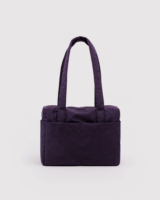 A dark purple canvas tote bag with two shoulder straps and a front pocket, photographed against a light gray studio background.