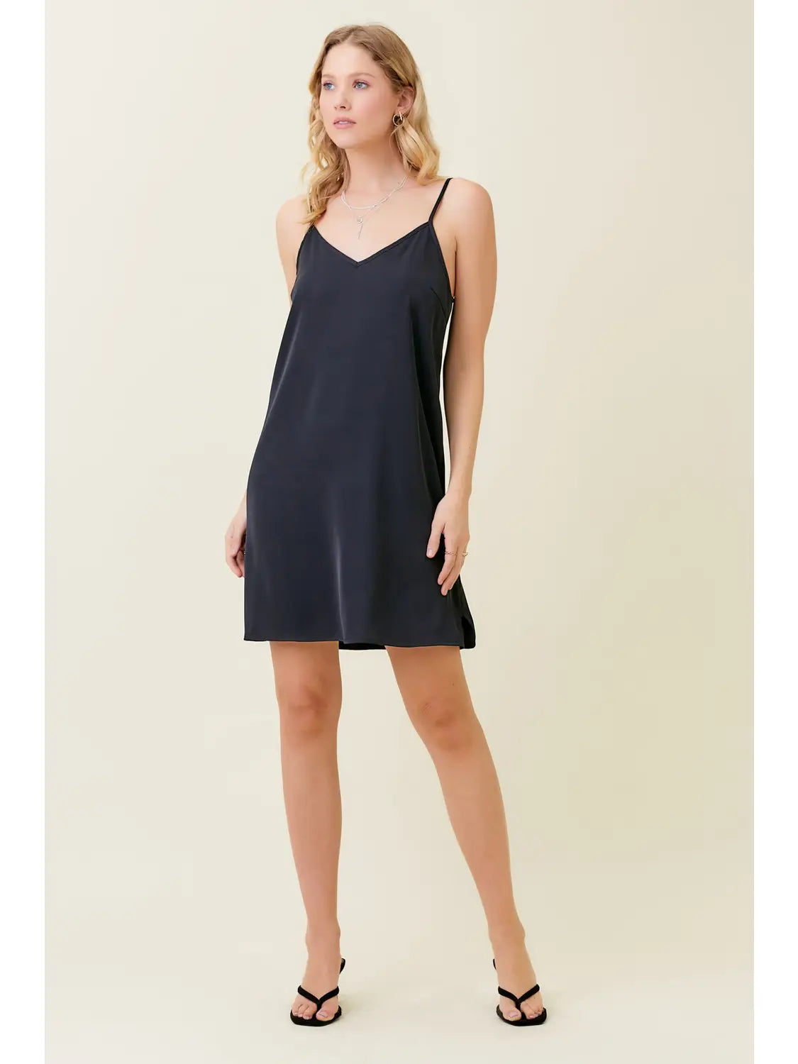 Woman wearing a black slip dress against a plain background
