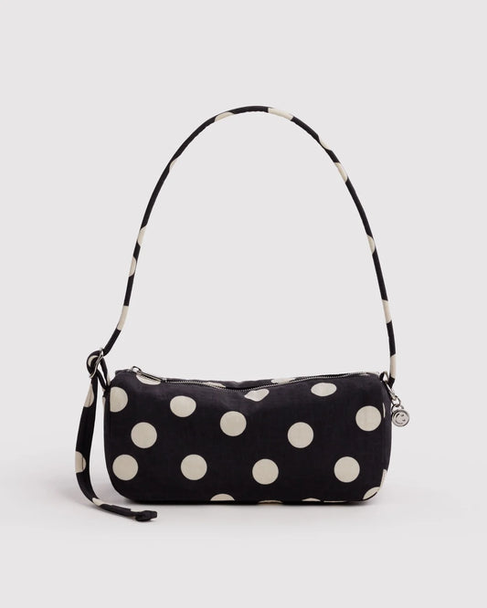A black fabric shoulder bag with large cream polka dots and a matching patterned strap, shown against a light gray studio background.