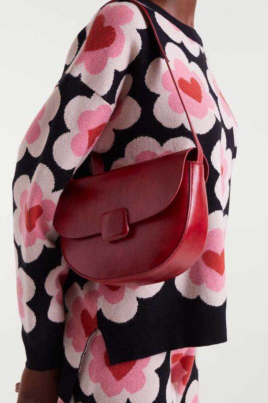 Red handbag worn by a person in a floral-patterned outfit