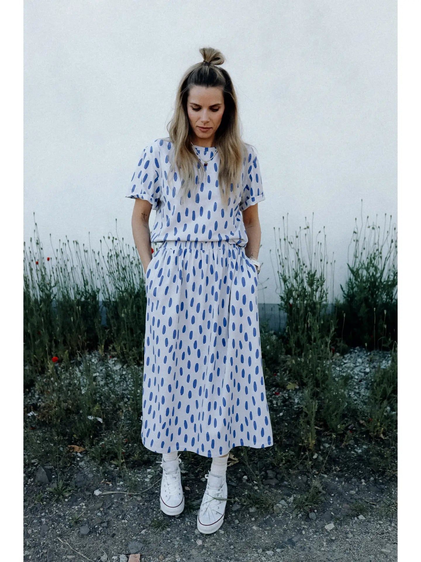 Woman wearing a white dress with blue patterns standing outdoors against a plain background