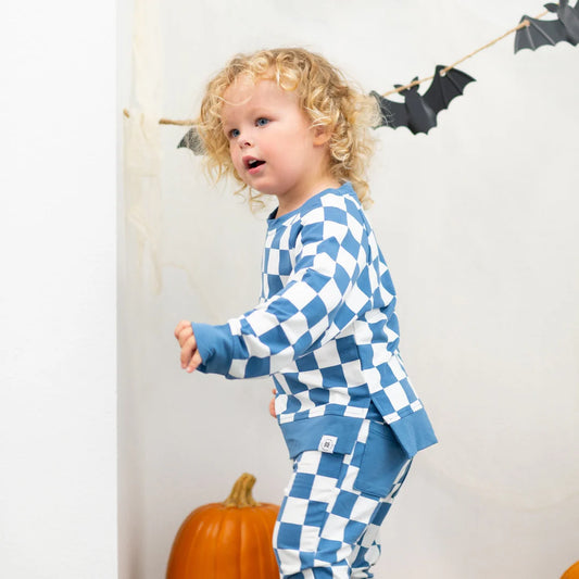 Child wearing blue and white checkered pajamas with Halloween decorations in the background.