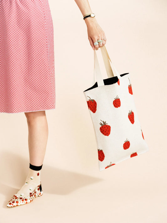 Person holding a tote bag with strawberry pattern on a beige background