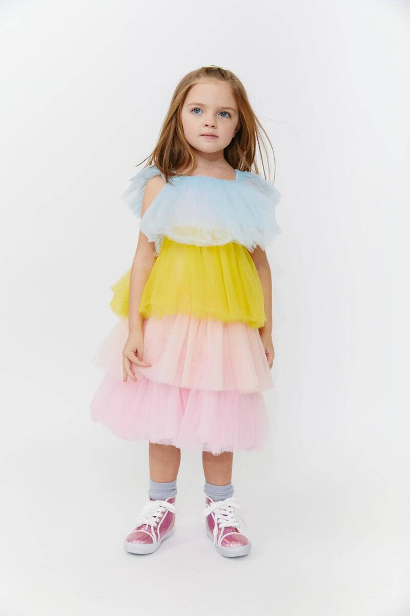 A young girl wearing a pastel-colored tiered tulle dress with short sleeves, standing against a white background by Lola and the Boys